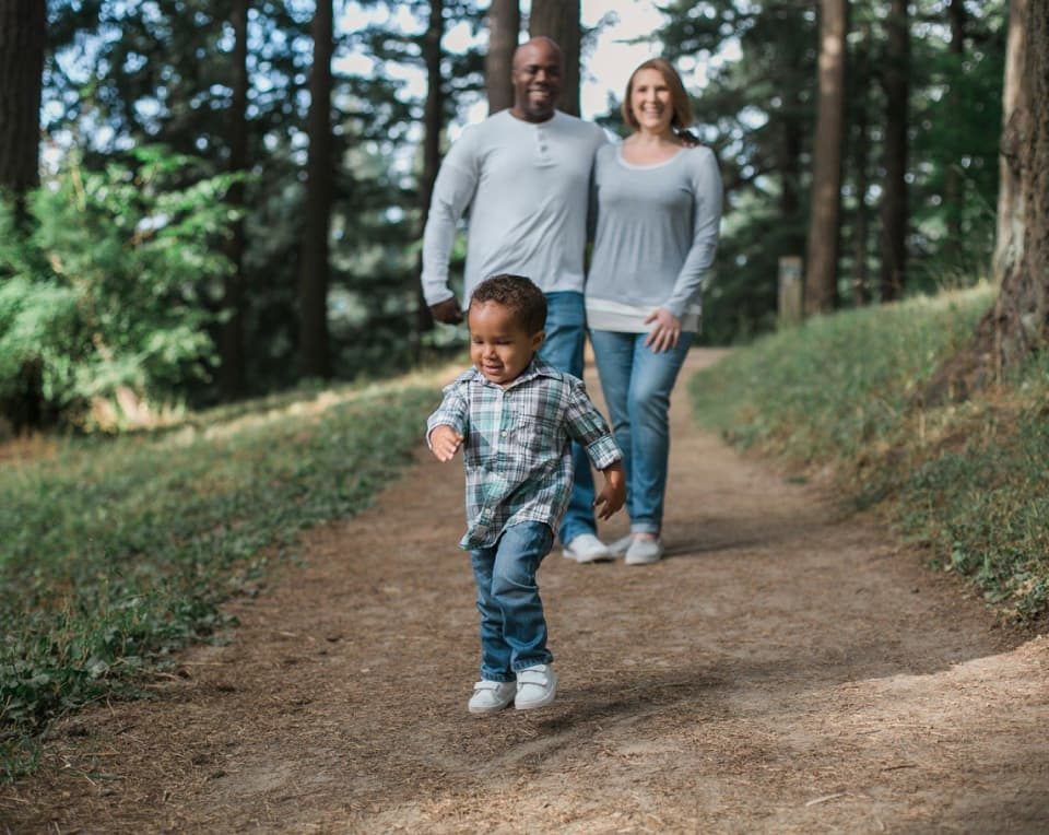 Family of 3 with a young child exploring on an outdoor trail in the woods